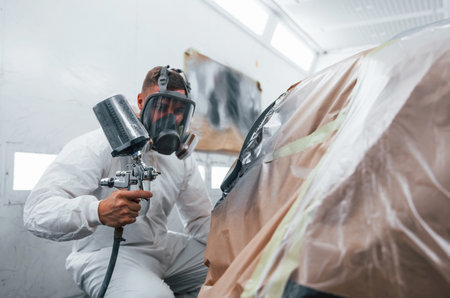 Painting job in progress. Caucasian automobile repairman in uniform works in garageの写真素材