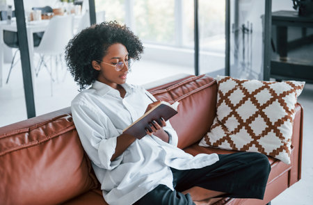 Holds notepad. Young african american woman with curly hair indoors at homeの写真素材