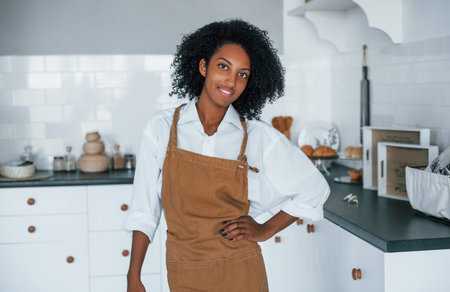 On the kitchen. Young african american woman with curly hair indoors at homeの写真素材