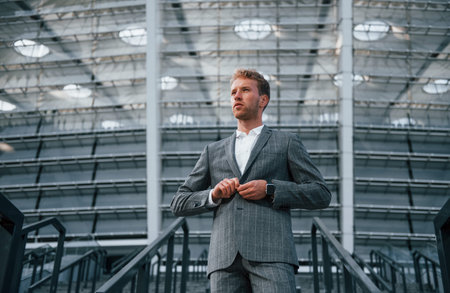 On the stairs of stadium. Young businessman in grey formal wear is outdoors in the city