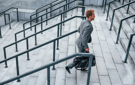 Holds bag in hands. Young businessman in grey formal wear is outdoors in the cityの写真素材