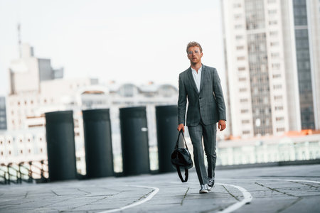Walks on the road. Young businessman in grey formal wear is outdoors in the cityの写真素材