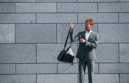 Against grey wall. Young businessman in grey formal wear is outdoors in the cityの写真素材