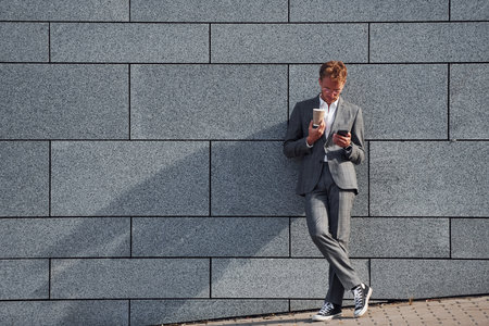 Against grey wall. Young businessman in grey formal wear is outdoors in the cityの写真素材