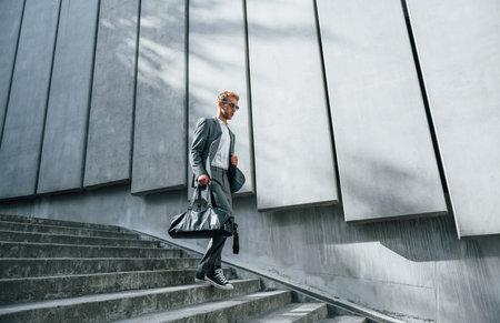 Going down by the stairs. Young businessman in grey formal wear is outdoors in the cityの写真素材