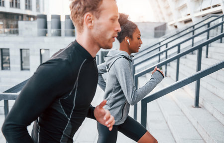 Running on bleachers. European man and african american woman in sportive clothes have workout togetherの写真素材
