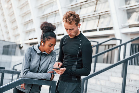 Using phone. European man and african american woman in sportive clothes have workout togetherの写真素材