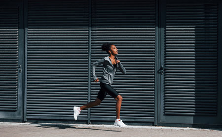 Side view of young african american woman in sportive clothes that runs near wallの写真素材