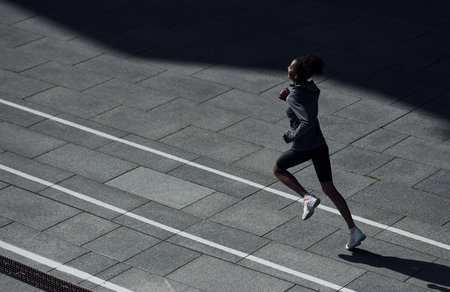 Fast runner. Young african american woman in sportive clothes have workout outdoors at daytimeの写真素材