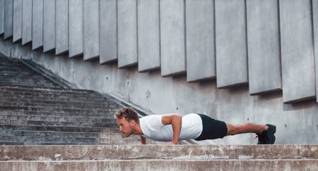 Against building exterior. Young man in sportive clothes have workout outdoors at daytimeの写真素材