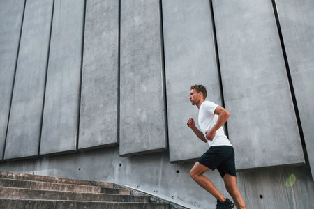 Against building exterior. Young man in sportive clothes have workout outdoors at daytimeの写真素材