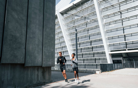 Near big wall. European man and african american woman in sportive clothes have workout togetherの写真素材