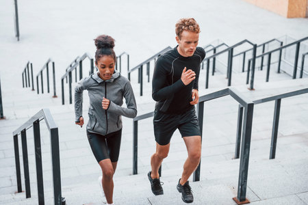 Running on bleachers. European man and african american woman in sportive clothes have workout togetherの写真素材
