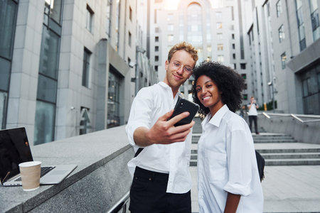 With phone in hands. Man with afrian american woman together in the city outdoorsの写真素材