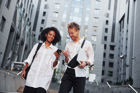 With phone in hands. Man with afrian american woman together in the city outdoorsの写真素材