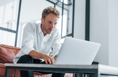 Caucasian young guy in elegant white shirt indoors at homeの写真素材