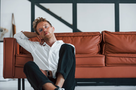Having a rest. Caucasian young guy in elegant white shirt indoors at homeの写真素材