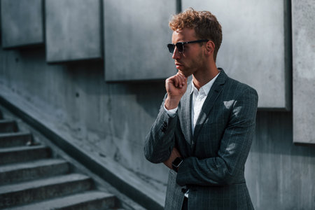 Young successful businessman in grey formal wear is outdoors in the cityの写真素材