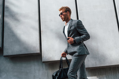 In sunglasses. Young successful businessman in grey formal wear is outdoors in the cityの写真素材