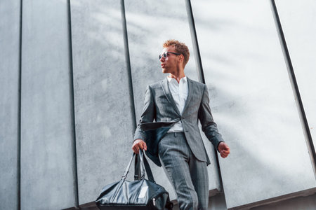 In sunglasses. Young successful businessman in grey formal wear is outdoors in the cityの写真素材
