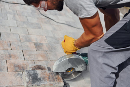 Uses circular saw. Male worker in yellow colored uniform have job with pavementの写真素材