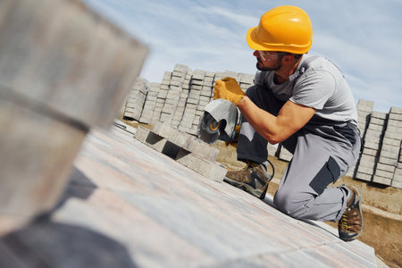 Slicing by circular saw. Male worker in yellow colored uniform have job with pavementの写真素材