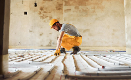 Worker in yellow colored uniform installing underfloor heating systemの写真素材