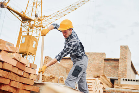 With shovel in hands. Construction worker in uniform and safety equipment have job on buildingの写真素材