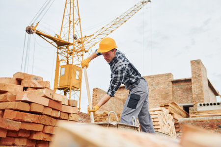 With shovel in hands. Construction worker in uniform and safety equipment have job on buildingの写真素材