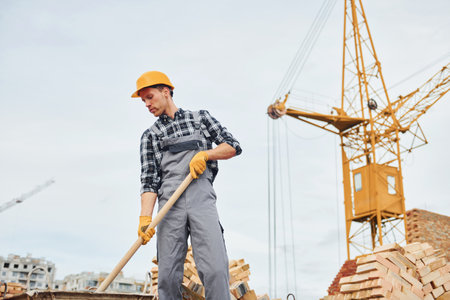 With shovel in hands. Construction worker in uniform and safety equipment have job on buildingの写真素材