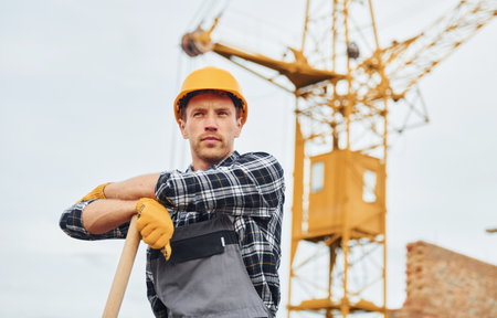 Using shovel with wooden holder. Construction worker in uniform and safety equipment have job on buildingの写真素材
