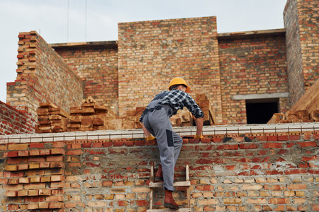Climbs up. Construction worker in uniform and safety equipment have job on buildingの写真素材