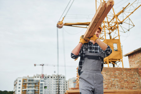 Transporting wooden boards. Construction worker in uniform and safety equipment have job on buildingの写真素材