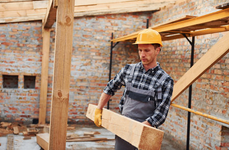 Transporting wooden boards. Construction worker in uniform and safety equipment have job on buildingの写真素材