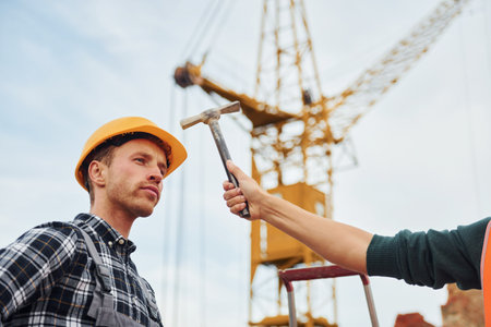 Man in yellow colored hard hat testing protection level. Hand holds hammerの写真素材