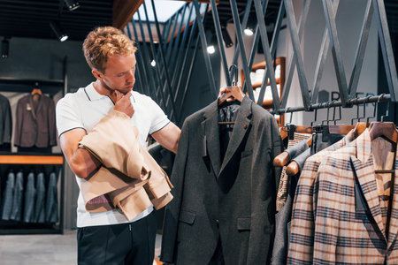 Looks for jacket. Young guy in modern store with new clothes. Elegant expensive wear for menの写真素材