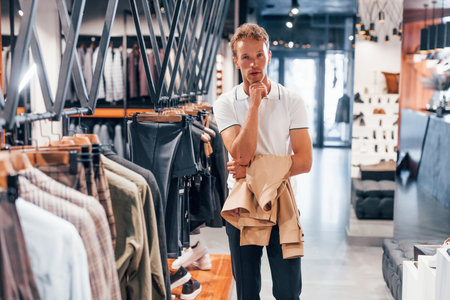 Looks for jacket. Young guy in modern store with new clothes. Elegant expensive wear for menの写真素材