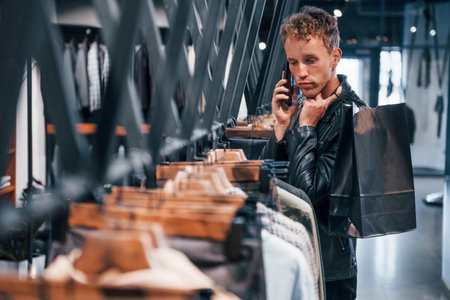 Talks by the phone. Young guy in modern store with new clothes. Elegant expensive wear for menの写真素材