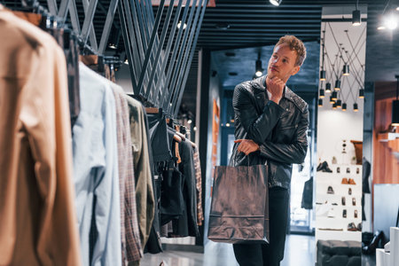 Big choice. Young guy in modern store with new clothes. Elegant expensive wear for menの写真素材