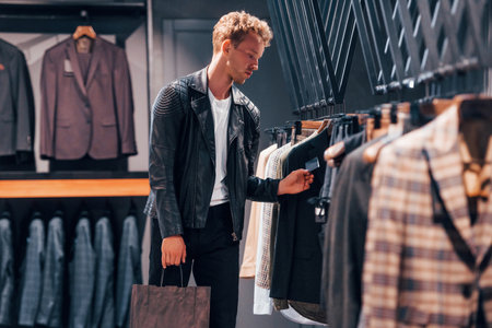 In beautiful black jacket. Young guy in modern store with new clothes. Elegant expensive wear for menの写真素材