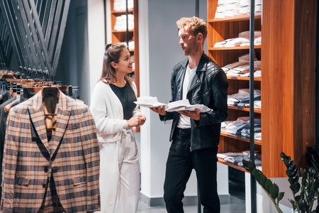 Young female worker helping guy to choose clothes in modern store with expensive wear for menの写真素材