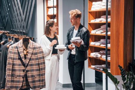 Young female worker helping guy to choose clothes in modern store with expensive wear for menの写真素材