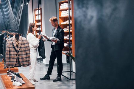 Young female worker helping guy to choose clothes in modern store with expensive wear for menの写真素材