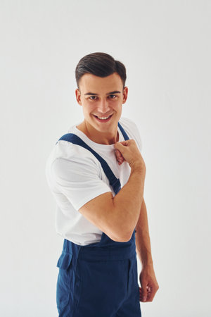 Shows biceps. Ready to work. Male worker in blue uniform standing inside of studio against white backgroundの写真素材