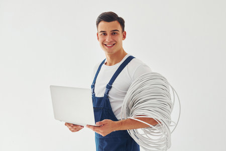 Uses laptop. Male worker in blue uniform standing inside of studio against white backgroundの写真素材