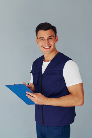 Writes in notepad. Male worker in blue uniform standing inside of studio against white backgroundの写真素材