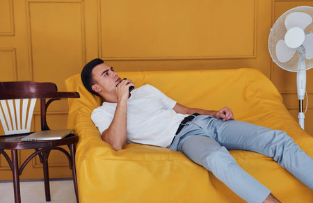 Young guy with stylish haircut and in casual clothes sitting indoors in room with orange colored interiorの写真素材