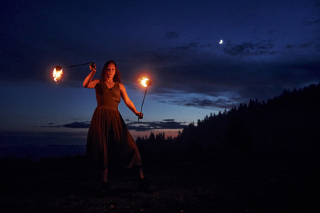 Fire show by woman in dress in night Carphatian mountains. Beautiful landscapeの写真素材