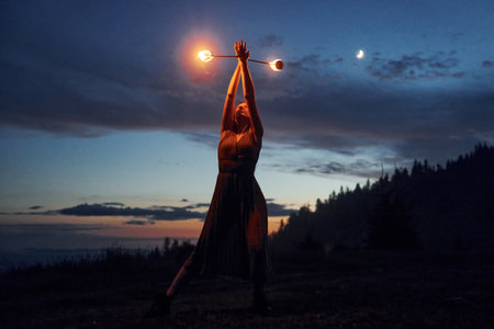 Fire show by woman in dress in night Carphatian mountains. Beautiful landscapeの写真素材