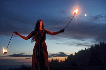 Fire show by woman in dress in night Carphatian mountains. Beautiful landscapeの写真素材